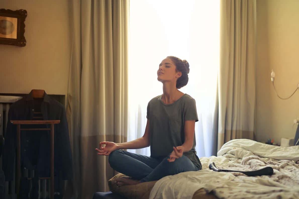 young woman sitting on bed meditating